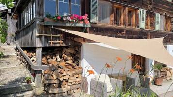 Une maison rustique en bois, dotée d’un balcon, d’une pile de bois de chauffage et d’un auvent en toile de couleur beige.