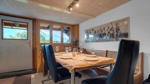 Comedor con una mesa de madera dispuesta para cuatro personas, rodeado de sillas negras, y vistas a la montaña a través de amplias ventanas.