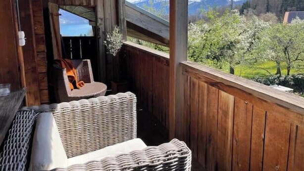Un balcón de madera con muebles de mimbre y vistas a montañas nevadas.