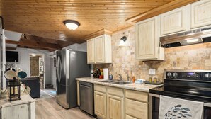 A kitchen with wooden cabinets, a stainless steel refrigerator, a stove, and a tiled backsplash.
