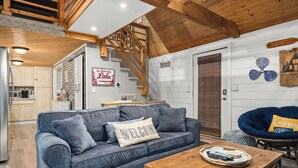 A cozy living room with a blue sofa, wooden coffee table, and a blue chair. A staircase leads to an upper level.