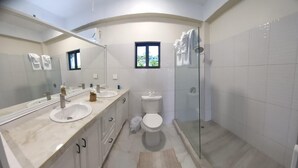 Un baño moderno con dos lavamanos, un inodoro y una ducha con mampara de vidrio.