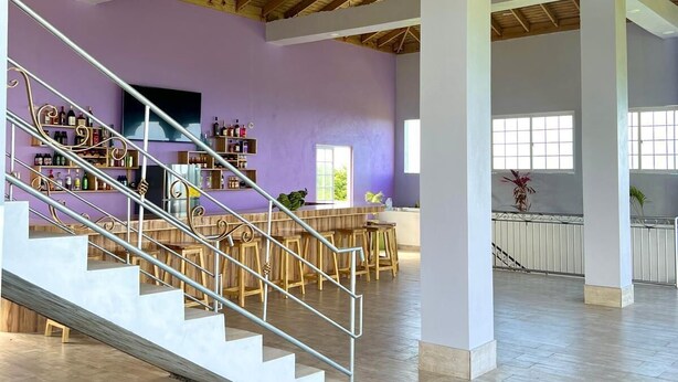 Un interior espacioso con un alto techo de madera, una escalera central y una zona de bar con estantes llenos de botellas.