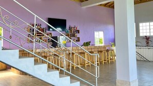 Un interior espacioso con techo alto, una escalera con barandillas metálicas y una zona de bar con taburetes y estantes llenos de botellas.