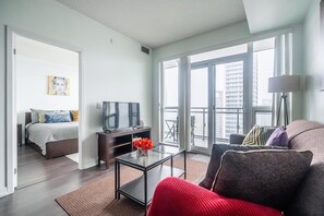 Un salon moderne comprenant un canapé, une table basse, un téléviseur et un balcon offrant une vue sur la ville.