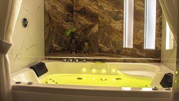 A bathtub with a yellowish water feature, a marble wall, and a window with curtains.