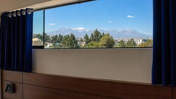 Un dormitorio con cama, ventana con cortinas, cabecero de madera y vistas a montañas.