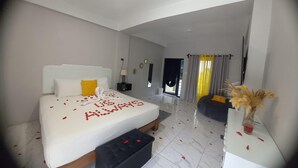 A modern hotel room with a large bed, a bedside table, a small sofa, and a view of the outside.