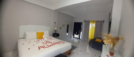 Una habitación de hotel moderna con una cama grande, una mesita de noche, un pequeño sofá y vistas al exterior.
