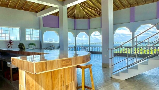 A spacious interior with a high ceiling, a central wooden bar, and a staircase leading to an upper level.