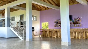 A spacious indoor area with a high ceiling, wooden beams, and a bar area with stools.