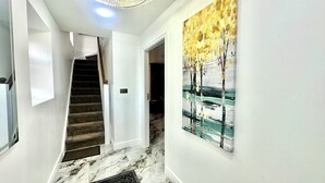 Un pasillo con suelo de mármol, una escalera y un cuadro abstracto grande en la pared.