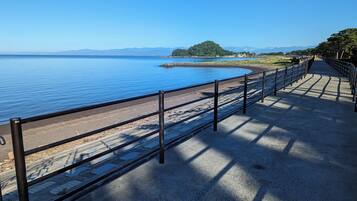 A coastal walkway with a metal railing, a paved path, and a view of the sea and distant mountains.
