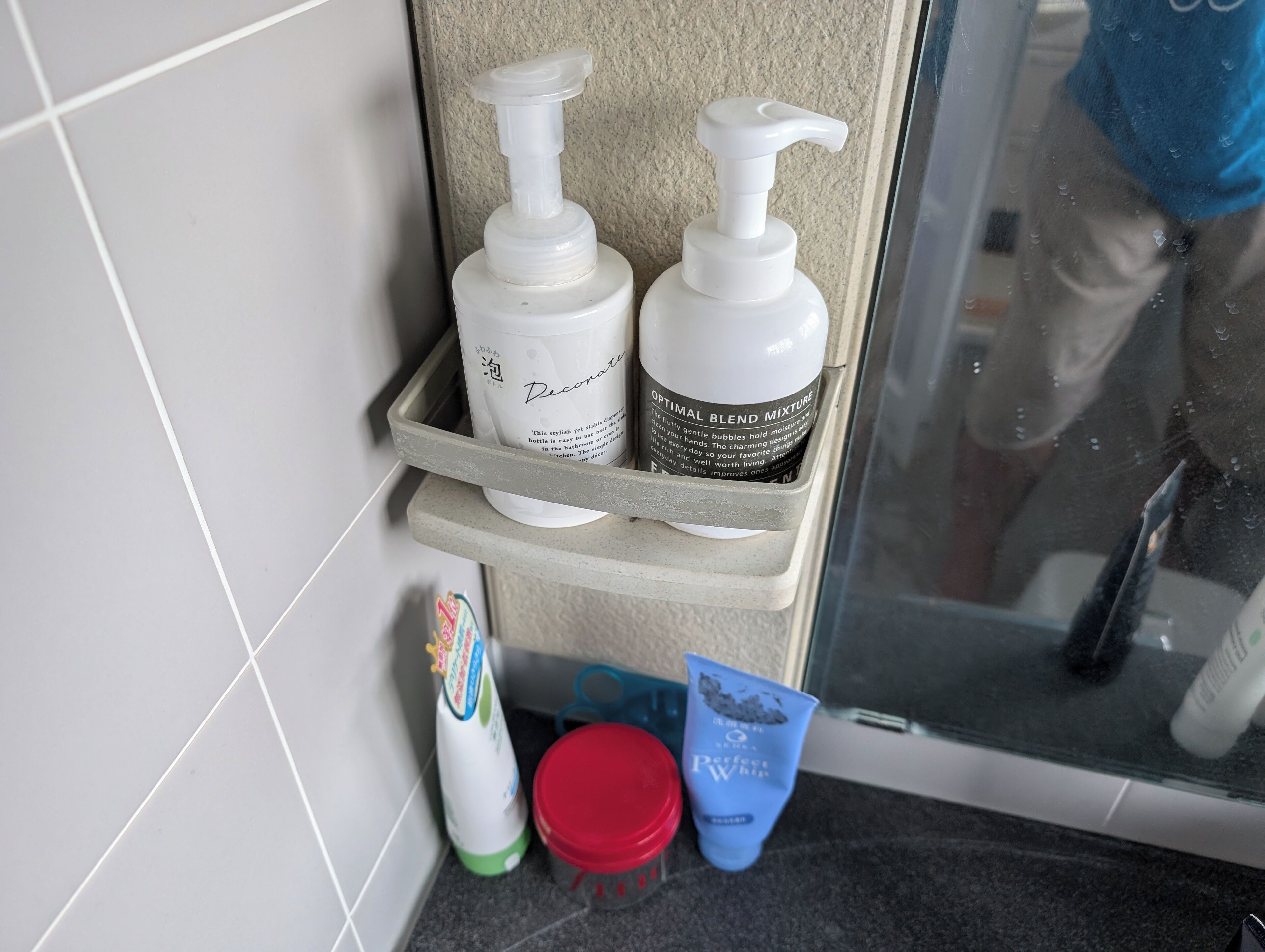 A bathroom shelf with toiletries including a bottle of lotion, a tube of cream, and a red container.