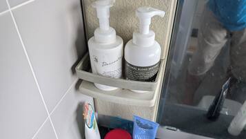A bathroom shelf with toiletries including a bottle of lotion, a tube of cream, and a red container.