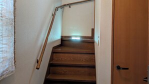 Una escala de fusta amb barana, una porta a la part inferior i un lluminari a la paret.