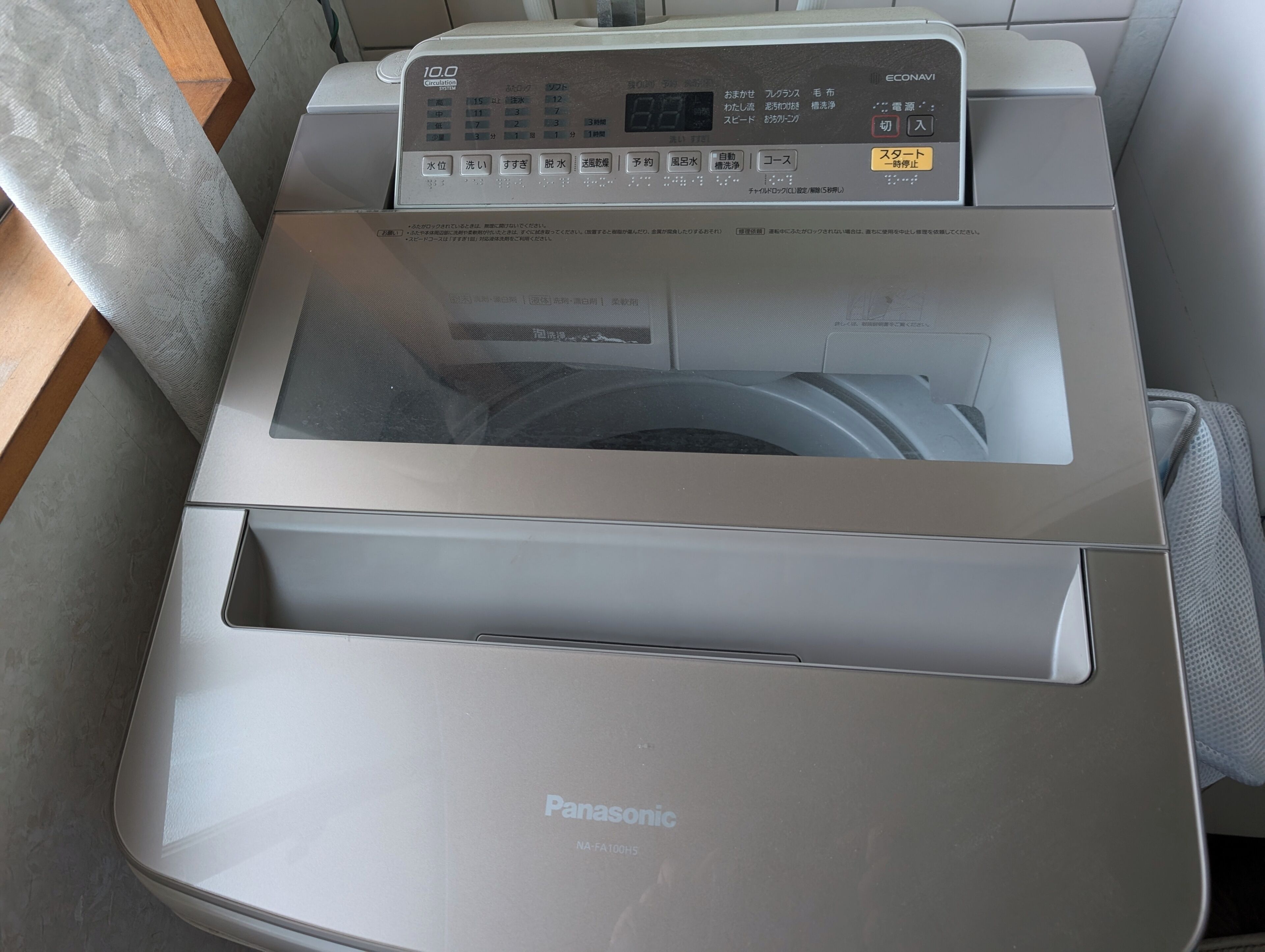 Uma máquina de lavar e secar Panasonic com painel de controle, porta transparente e bandeja frontal para saída de papel.