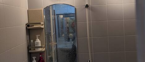 Un baño con ducha, inodoro y espejo.