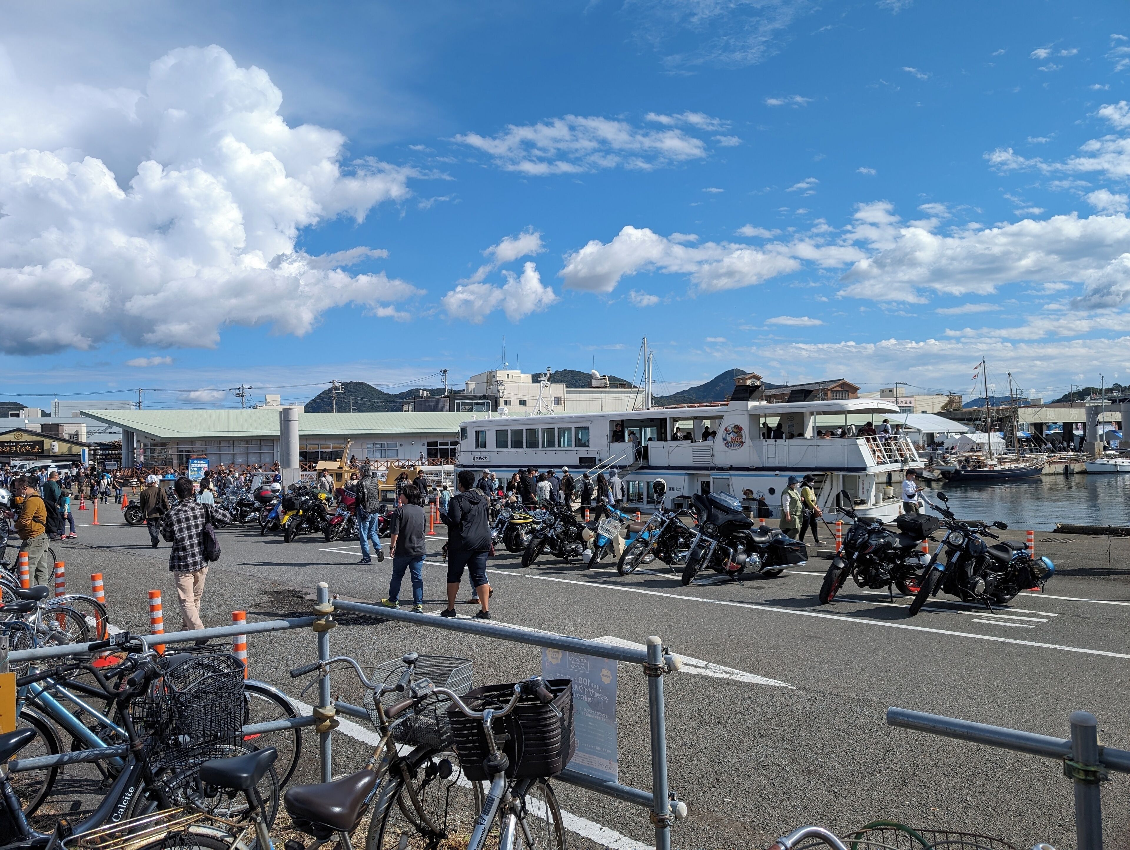 En travl havn med både, en menneskemængde og parkerede motorcykler.