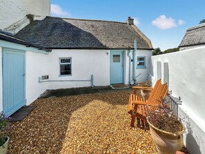 A white building with a blue door and window, a gravel driveway, and a wooden chair.