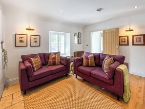 A living room with two purple sofas, a woven rug, framed pictures, and a radiator. - 1 bedroom accommodation in Whithorn, near Wigtown (Whithorn, near Wigtown)
