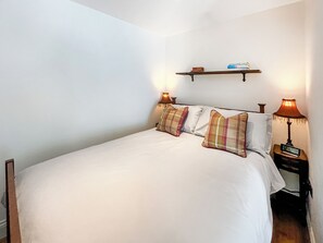 A neatly made bed with a white duvet, two bedside lamps, and a shelf above the bed. - 1 bedroom accommodation in Whithorn, near Wigtown (Whithorn, near Wigtown)