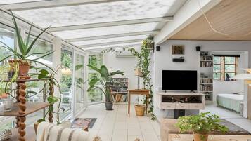 En rummelig stue med stort tv, bogreoler og mange planter.