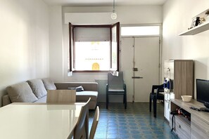 Un espacio habitable compacto con sofá, mesa de comedor, sillas, televisor y armario.