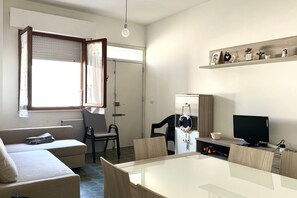 A compact living space with a sofa, dining table, chairs, a television, and a shelf with decorative items.