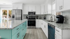 Una cucina moderna con mobili bianchi, un frigorifero in acciaio inossidabile, un forno a microonde, un fornello e una lavastoviglie.