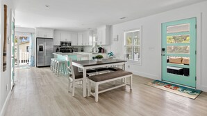 Una cucina moderna con mobili bianchi, un frigorifero in acciaio inossidabile e un'area pranzo con tavolo e sedie in legno.