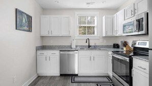 A modern kitchen with white cabinets, a dishwasher, a sink, a stove, and a microwave. - Entire Home - Great Location (Charleston)