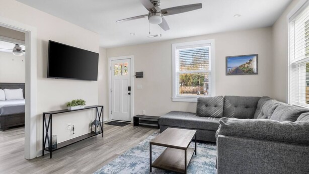 A modern living room with a grey sofa, a coffee table, and a TV mounted on the wall. - Entire Home - Great Location (Charleston)