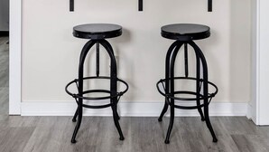 A kitchen area with a white wall, a wooden shelf, two black stools, and decorative wall mirrors. - Entire Home - Great Location (Charleston)