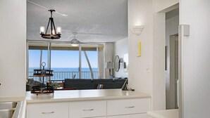 A modern kitchen with white cabinets, a dining area with a view of the ocean, and a ceiling fan. - Beautifully Upgraded, Amazing Ocean Views MS316 (Kihei)