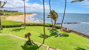 A well-maintained lawn with a few palm trees, a stone wall, and a view of the ocean. - Beautifully Upgraded, Amazing Ocean Views MS316 (Kihei)