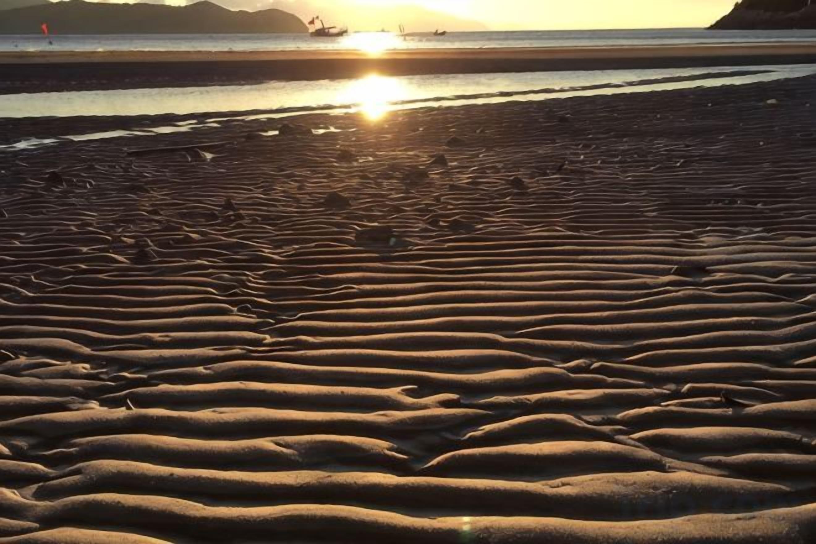 A beach with rippled sand patterns and a sunset in the background.