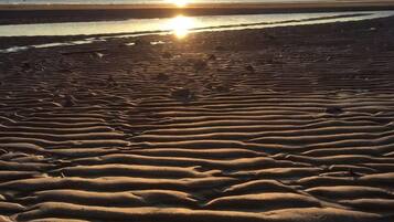 A beach with rippled sand patterns and a sunset in the background.