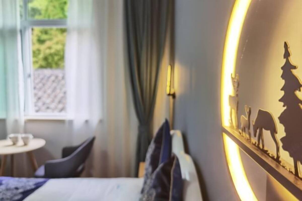 Ett hotellrum med en säng, ett litet bord med koppar, ett fönster med gardiner och en vägg med en siluettdekor.