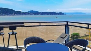 Een balkon met uitzicht op strand en bergen, met buitenmeubels en een tafel.