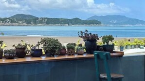 Een balkon met verschillende potplanten met uitzicht op een strand en bergen.