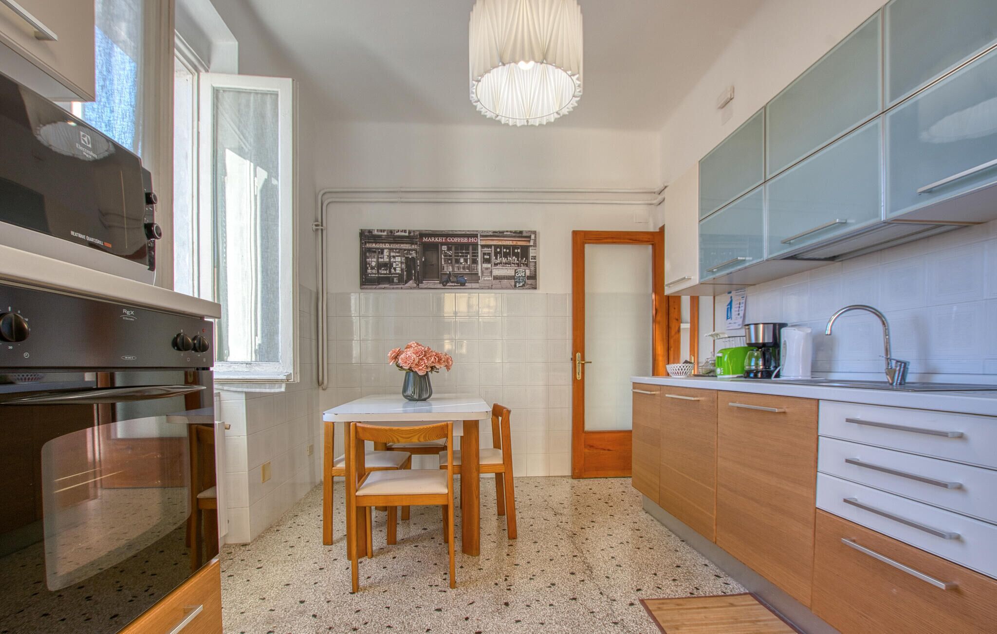 A kitchen with a stove, sink, and cabinets. There is a table with chairs and a vase of flowers.