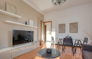 A modern living room with a flat-screen TV, a glass dining table, and a sofa.