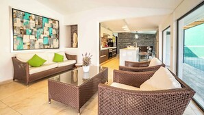 A modern living room with a glass coffee table, wicker furniture, a sofa with green cushions, and a large abstract painting on the wall. - Spacious House Pool & Jacuzzi (Xochitepec)