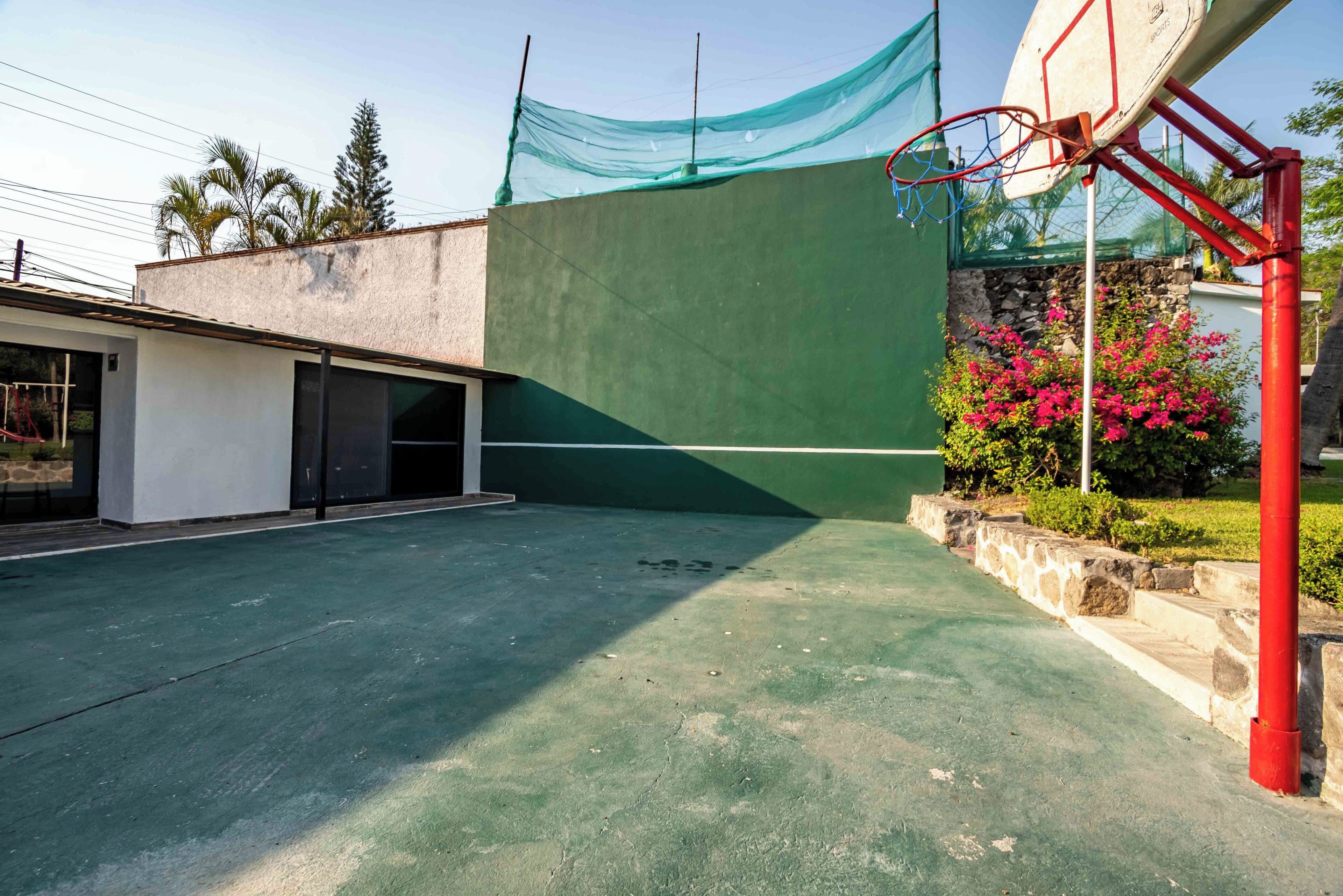 Una cancha de baloncesto al aire libre con superficie verde, aro rojo y red.