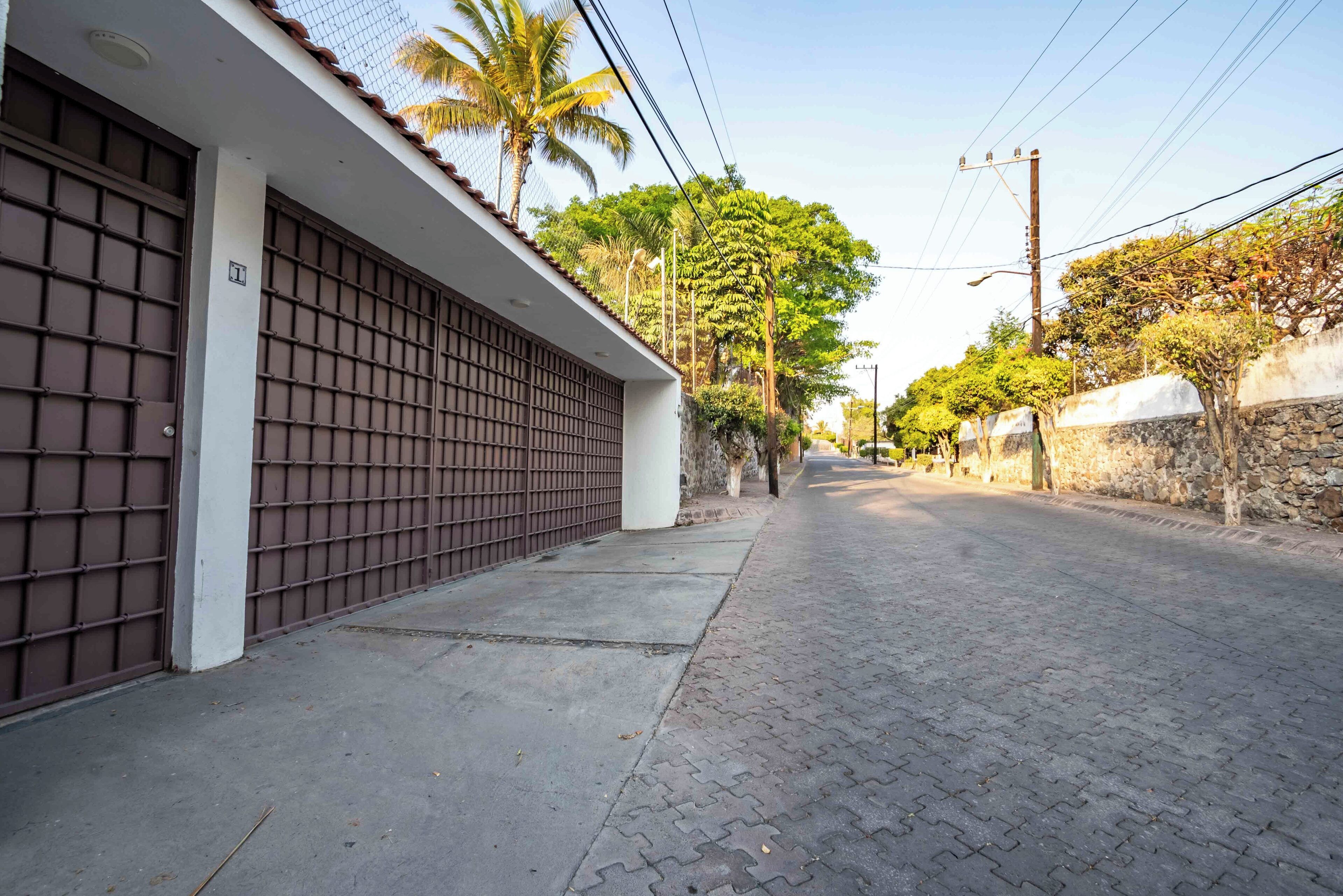 A quiet street with a gated building, paved sidewalks, and trees.