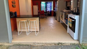 Cocina compacta con barra, refrigerador, horno y mesa de comedor con sillas.