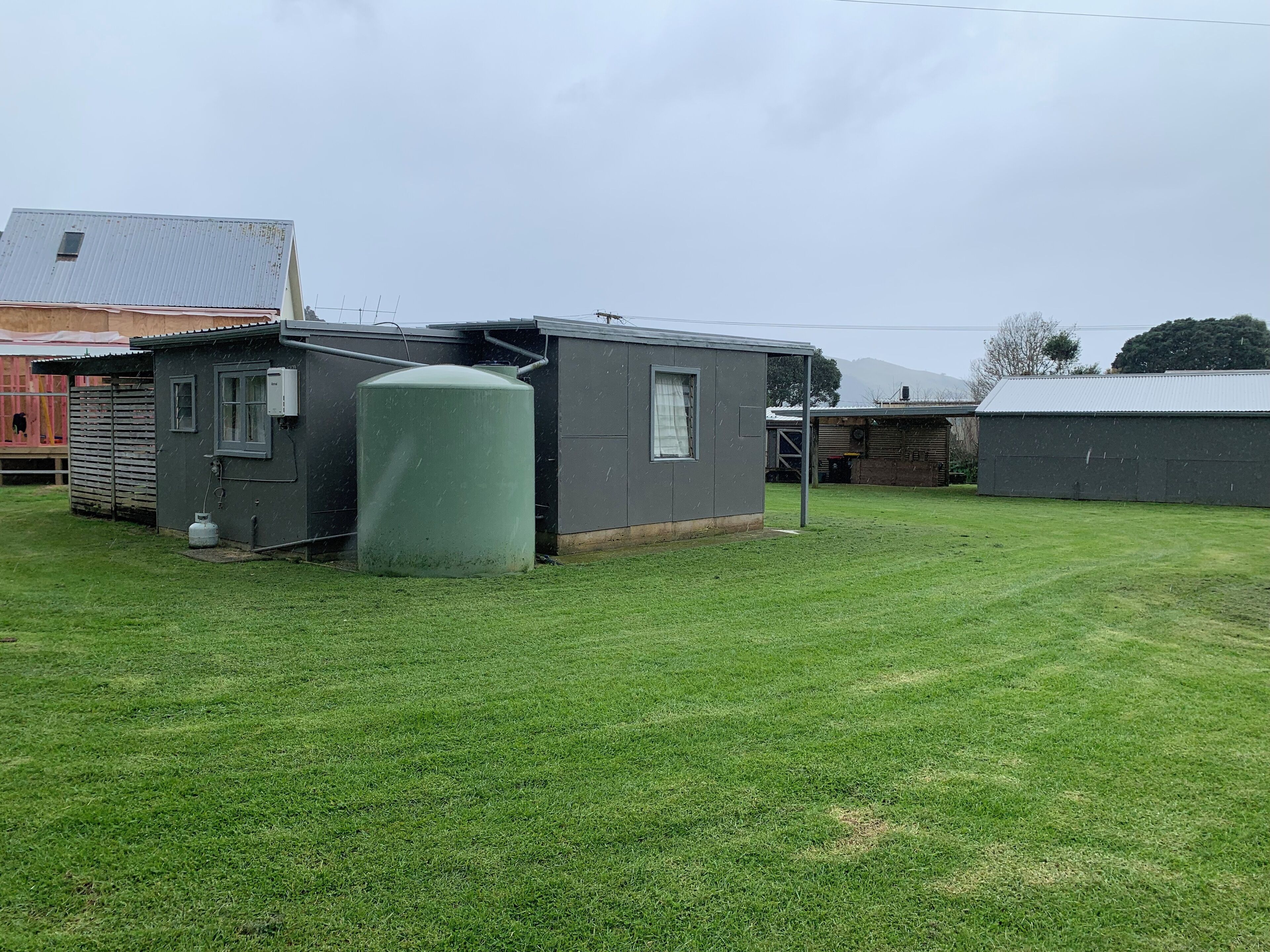 A small, single-story building with a metal roof, a large cylindrical tank, and a grassy yard.