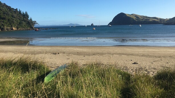 Una playa con agua cristalina, barcos y colinas al fondo.