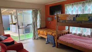 Una habitación con literas, un sofá, un televisor y una puerta corrediza de vidrio que da a un patio.